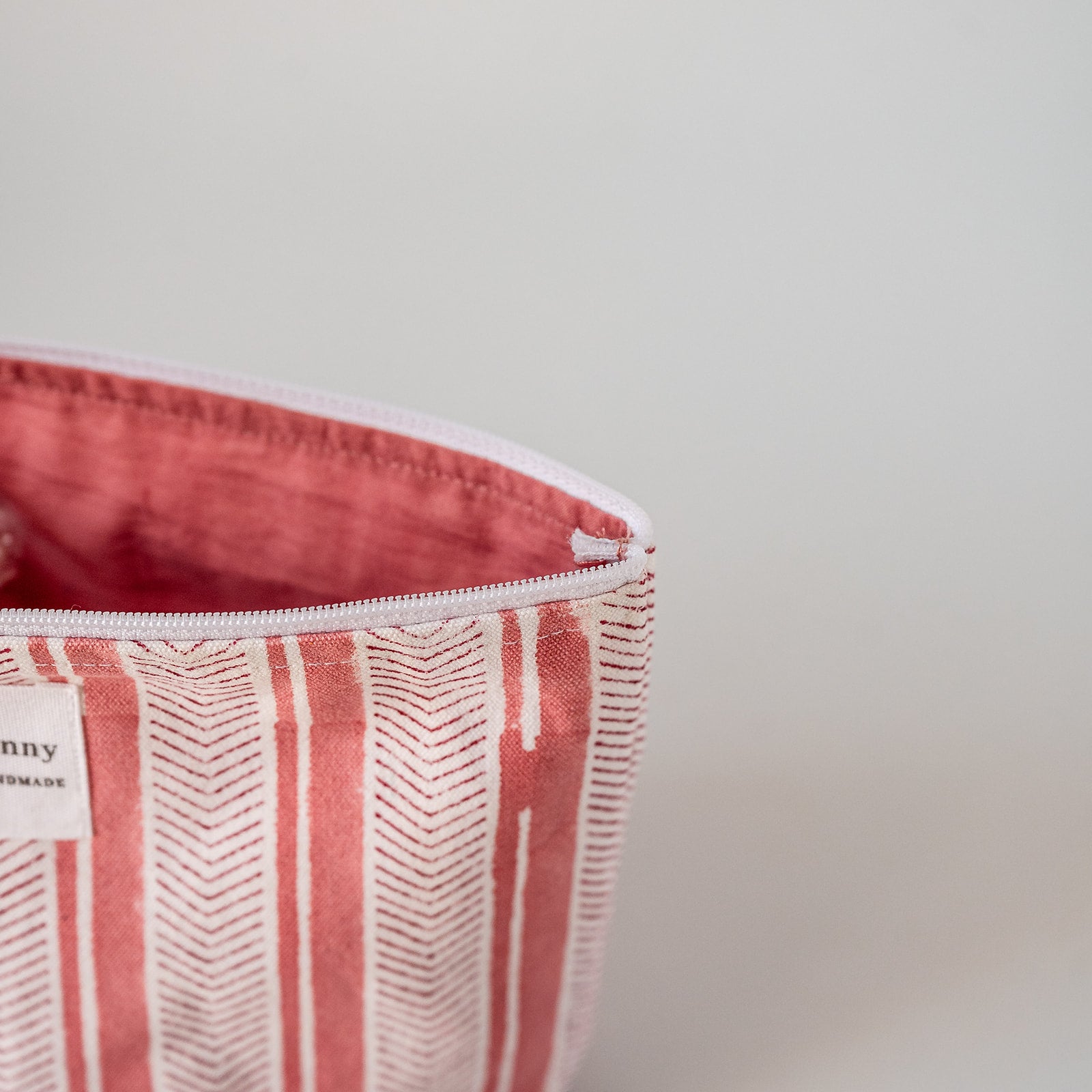 Close-up of a zippered pouch with a coral pink and white striped pattern, showing the interior lining and a small sewn label.