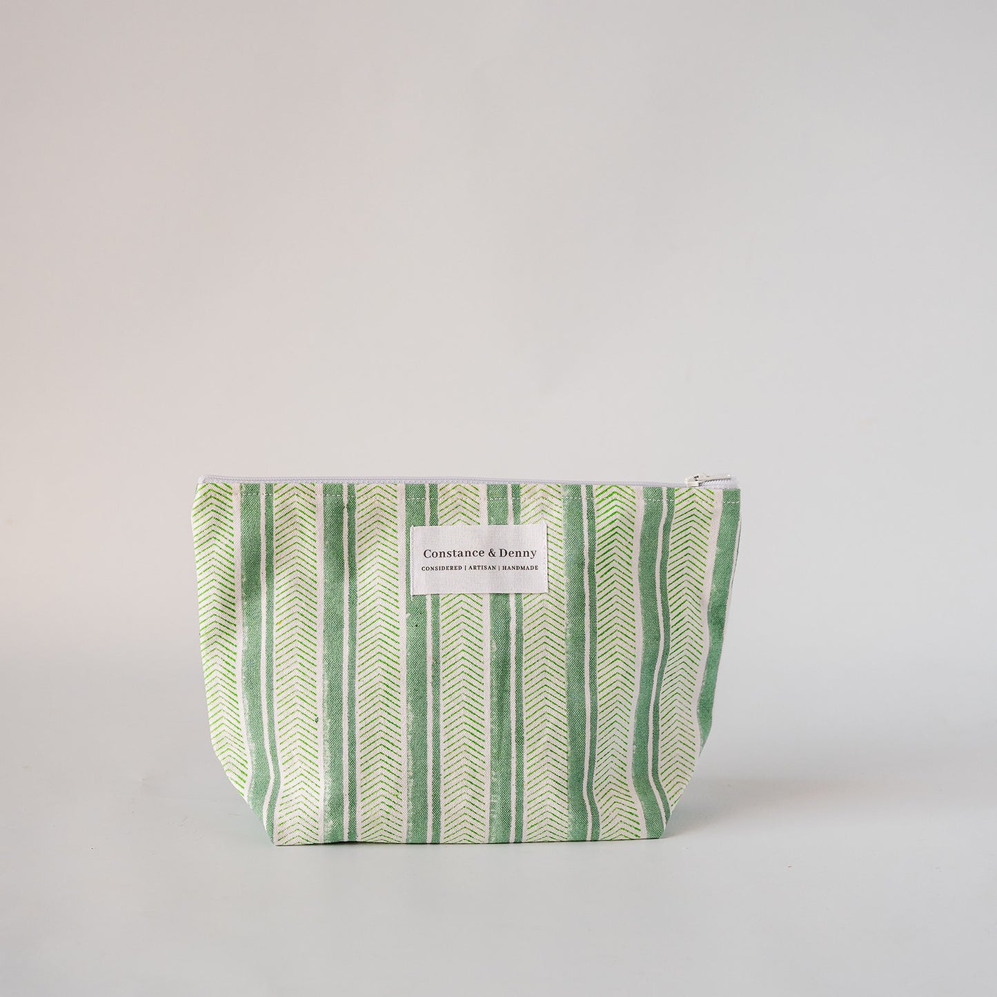A small zippered cosmetic pouch with a green and white herringbone pattern, featuring a white label that reads 'COSTUME & BEAUTY'.