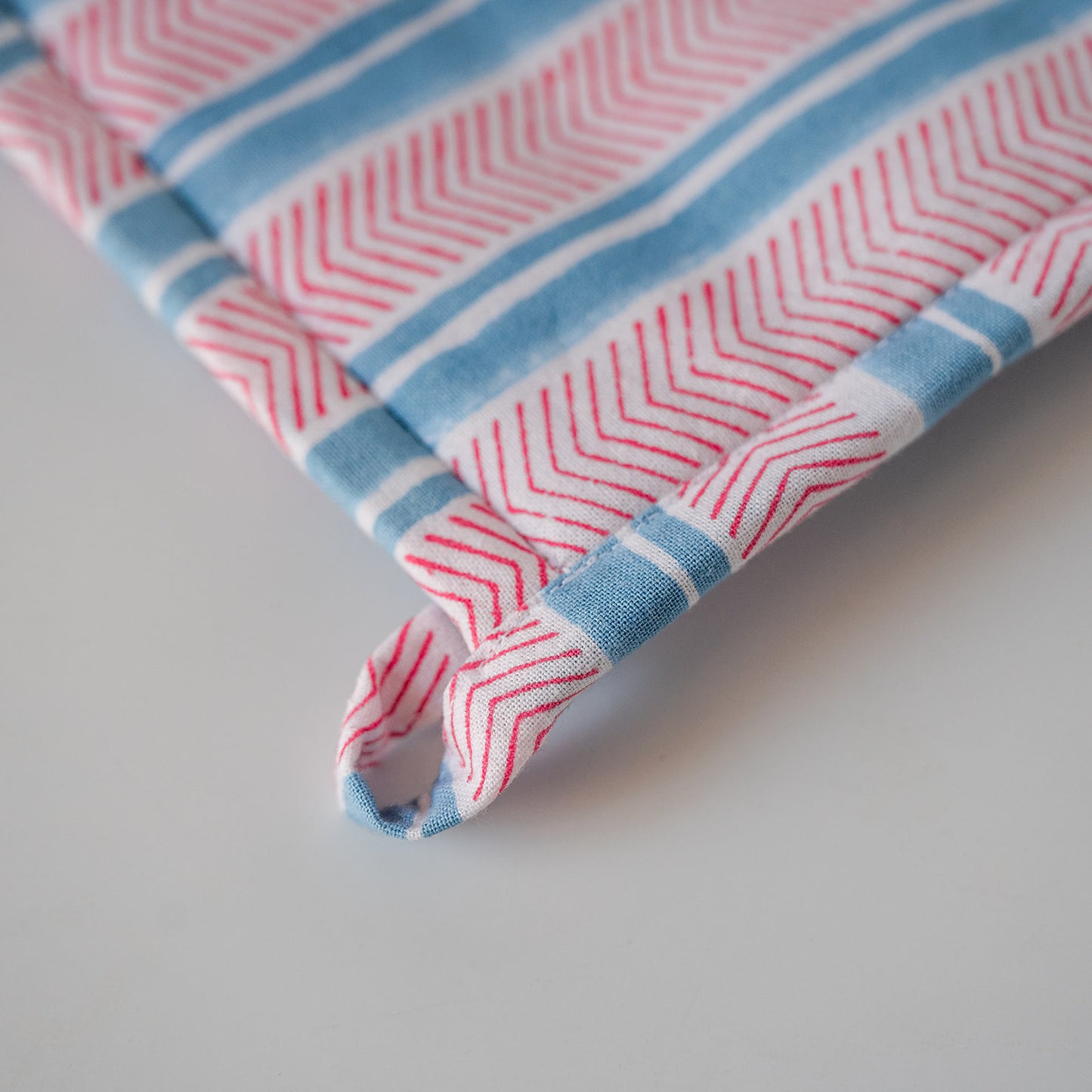 A close-up of a striped fabric product, likely a towel or cloth napkin, featuring red and white chevron patterns and light blue stripes, with a matching fabric loop tab.
