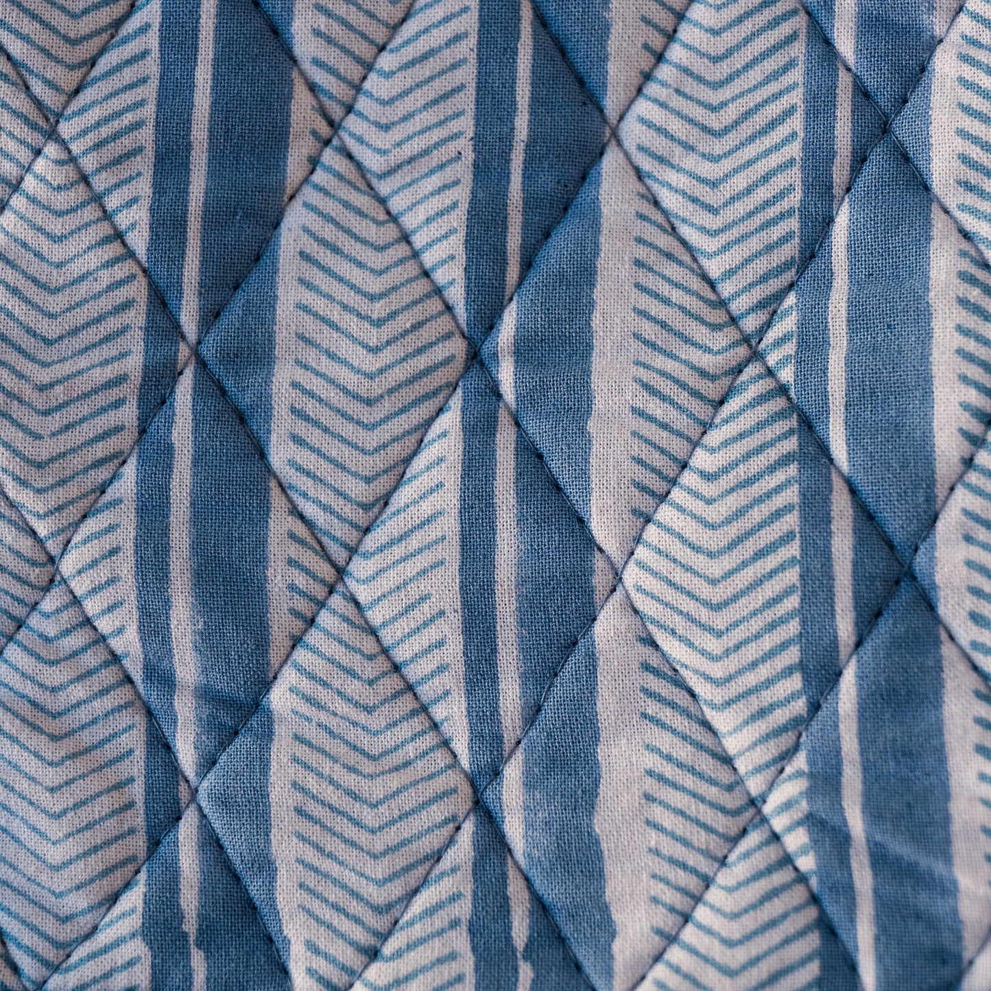 A close-up of a quilted fabric with a geometric pattern of blue, navy, and white stripes and chevrons.