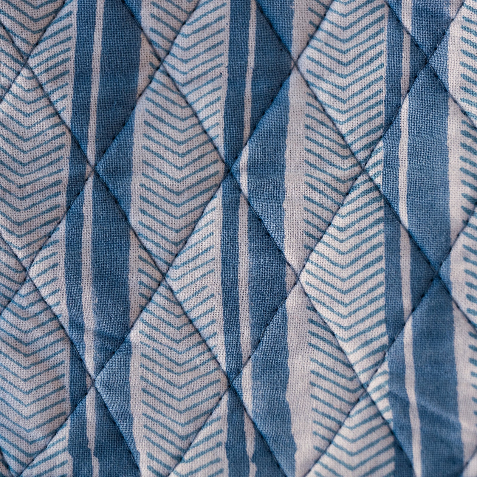 A close-up of a quilted fabric with a geometric pattern of blue, navy, and white stripes and chevrons.
