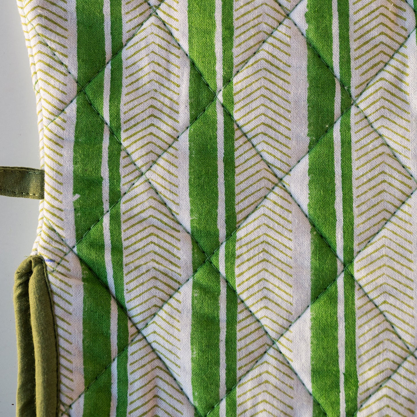 Close-up of a quilted fabric item, likely an oven mitt or cushion cover, featuring a green and white striped pattern with a diamond-quilted design.