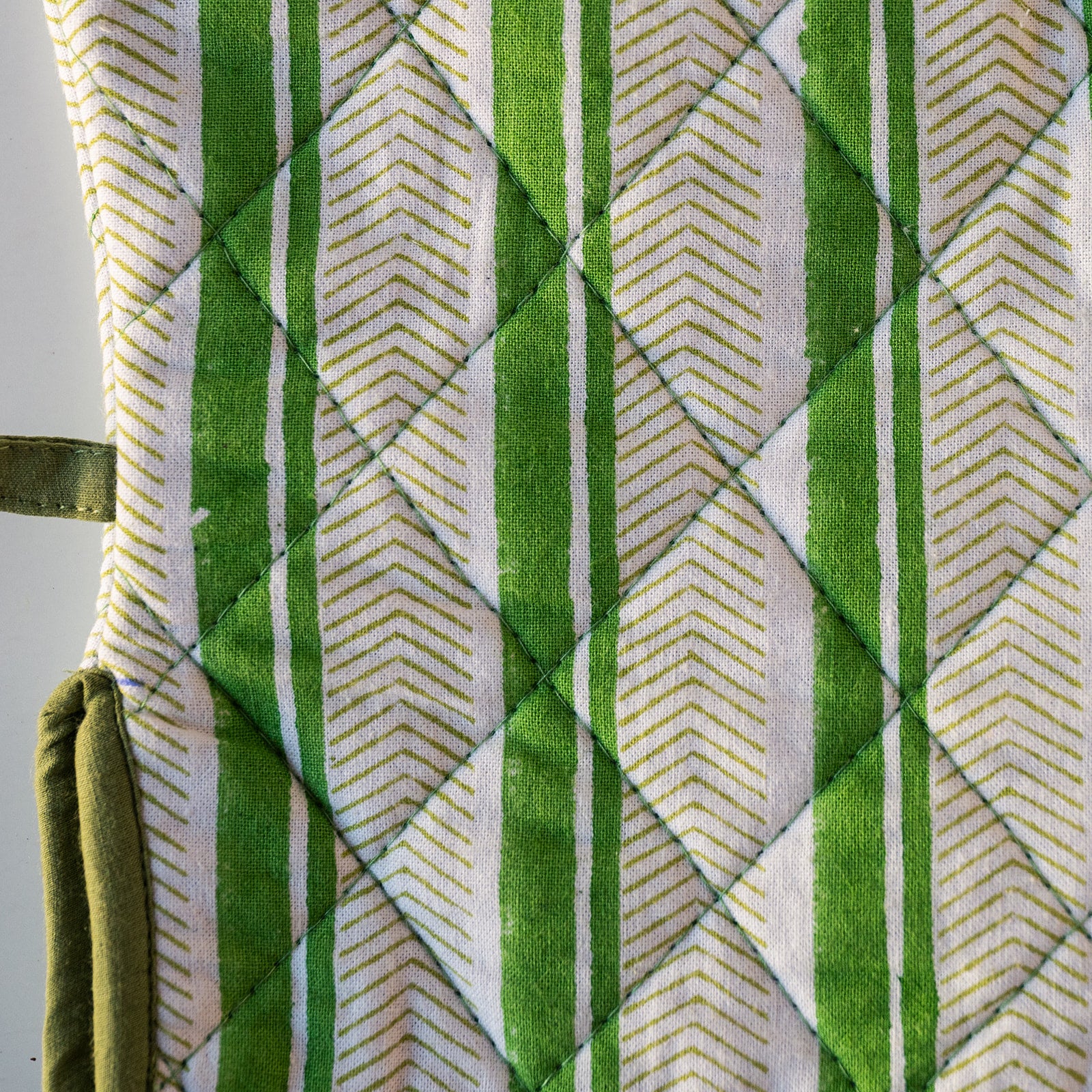 Close-up of a quilted fabric item, likely an oven mitt or cushion cover, featuring a green and white striped pattern with a diamond-quilted design.