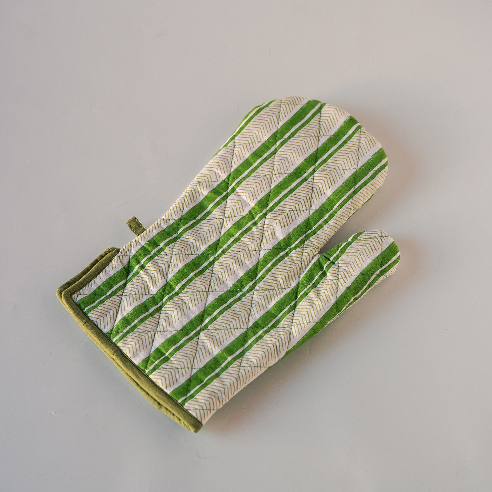 A single quilted oven mitt with a green and white striped pattern and olive green trim, photographed on a neutral light gray background.