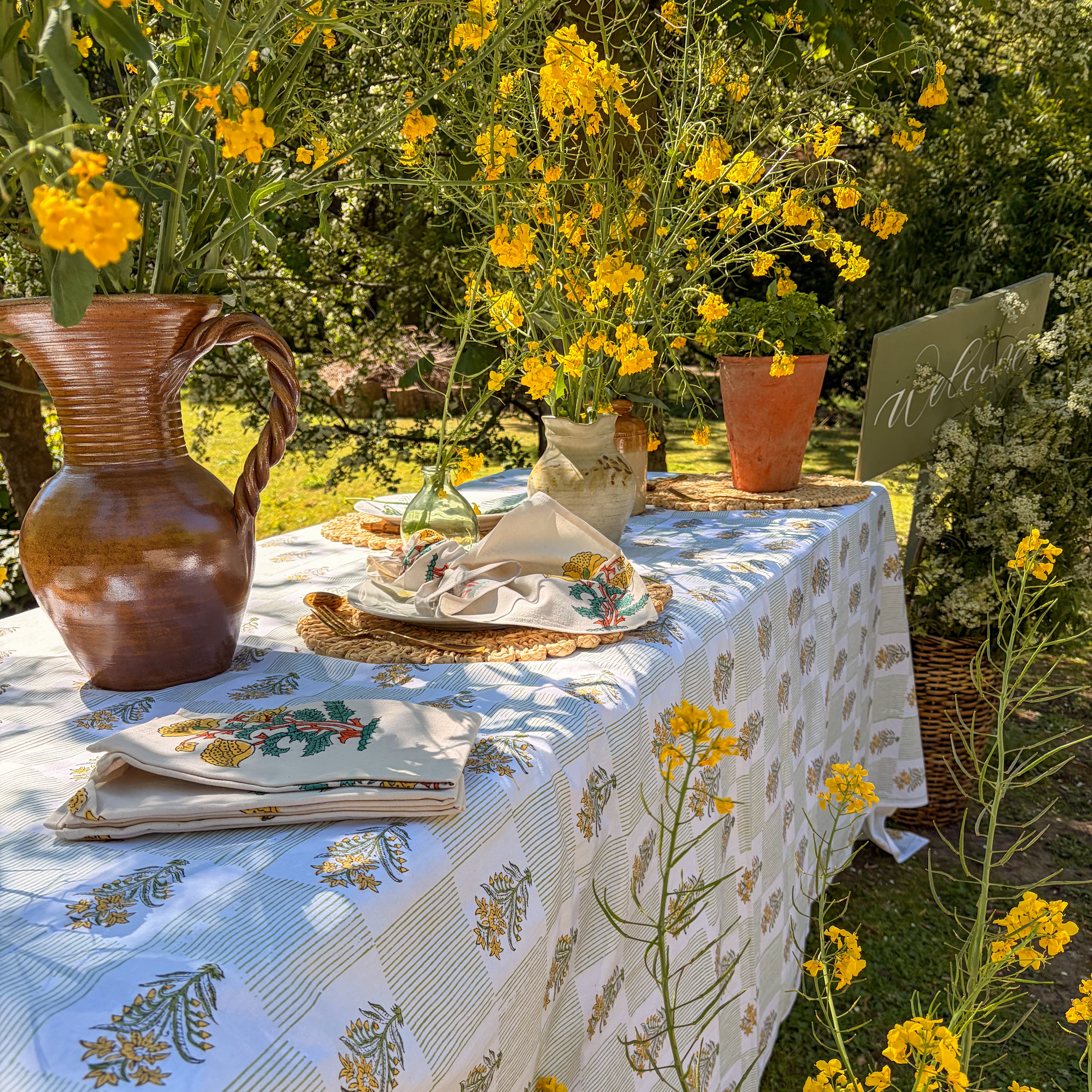 Outdoor table setting with floral tablecloth, yellow flowers, and rustic decor.