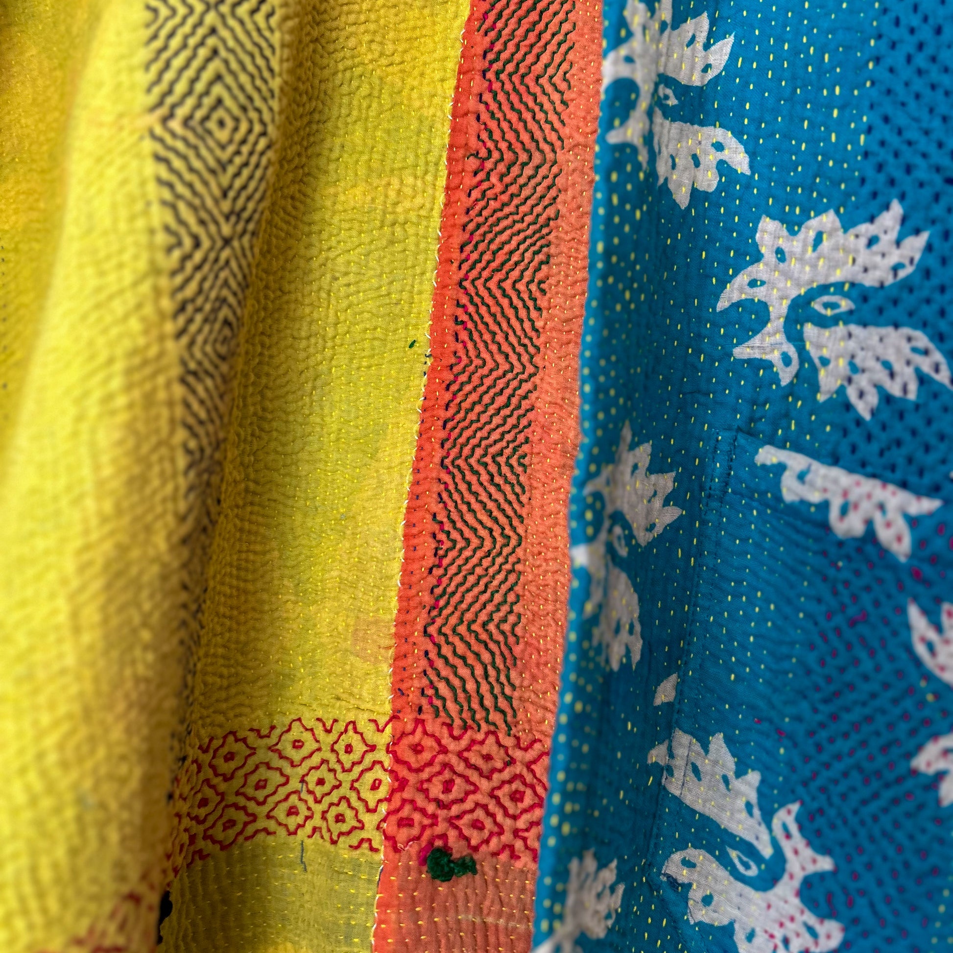 Close-up of colorful fabric with patterns in yellow, red, and blue. te floral patterns on a white background. Vintage-kantha-jacket-handmade-unique-38-turquoise-pattern-stitching-details