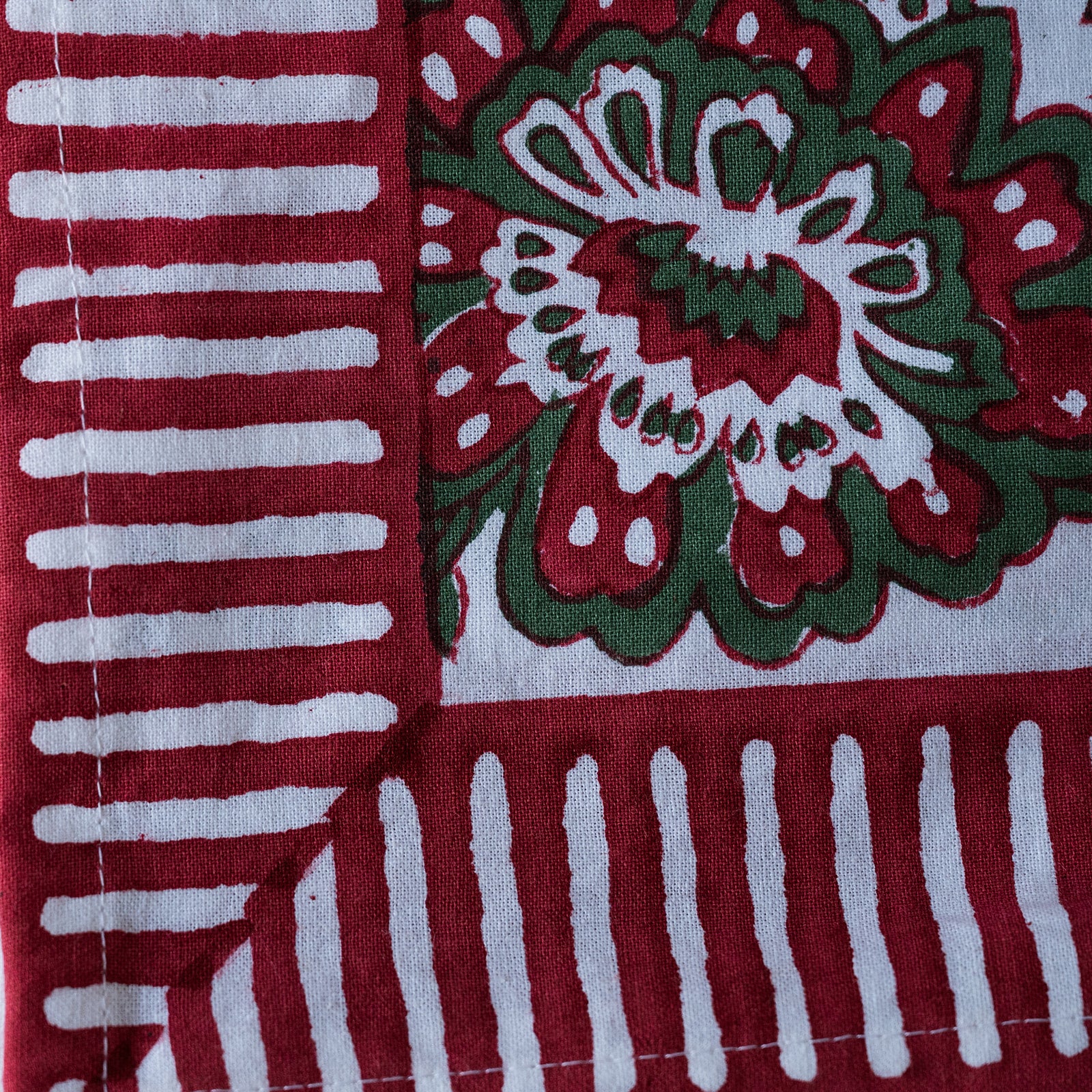 A close-up of a block-printed textile showing a red and green floral motif on a white base, alongside red and white striped sections.