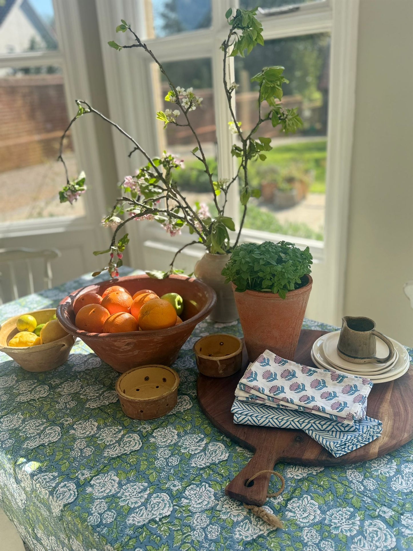 Table setting with fruits, plants, and tableware in a bright room.