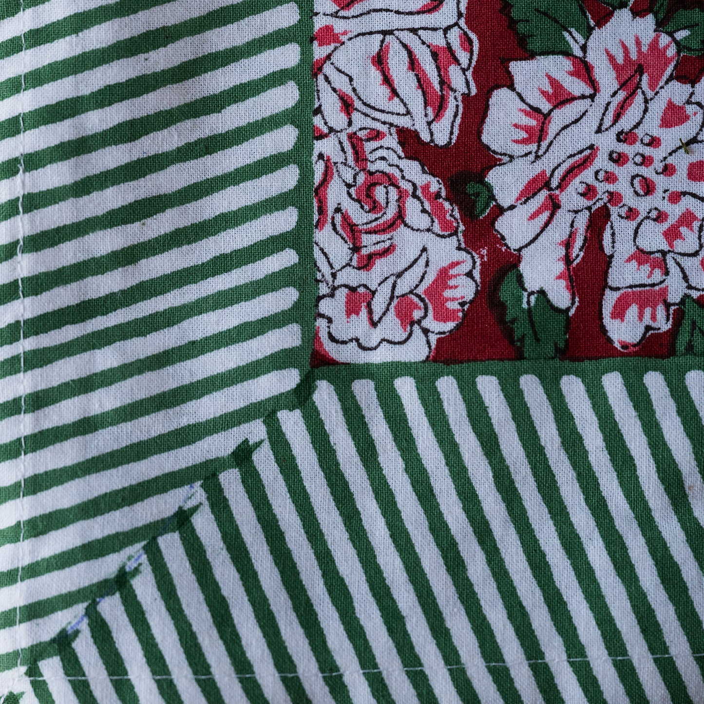 A close-up of a quilted fabric showing three distinct patterned sections: green and white stripes, a green and white striped corner, and a red, white, and green floral pattern.