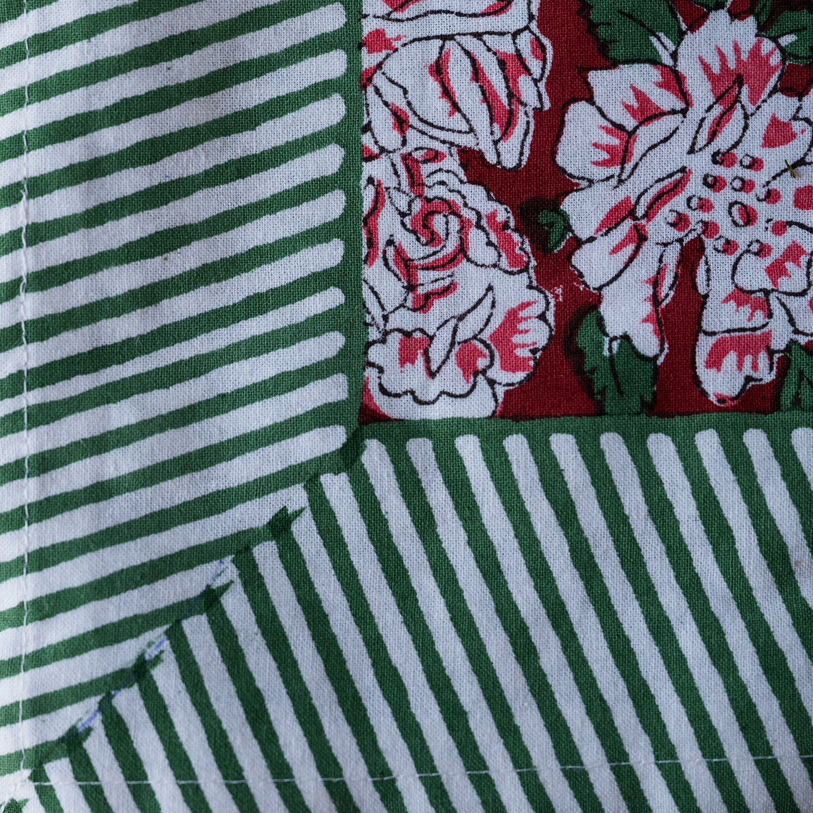 A close-up of a quilted fabric showing three distinct patterned sections: green and white stripes, a green and white striped corner, and a red, white, and green floral pattern.