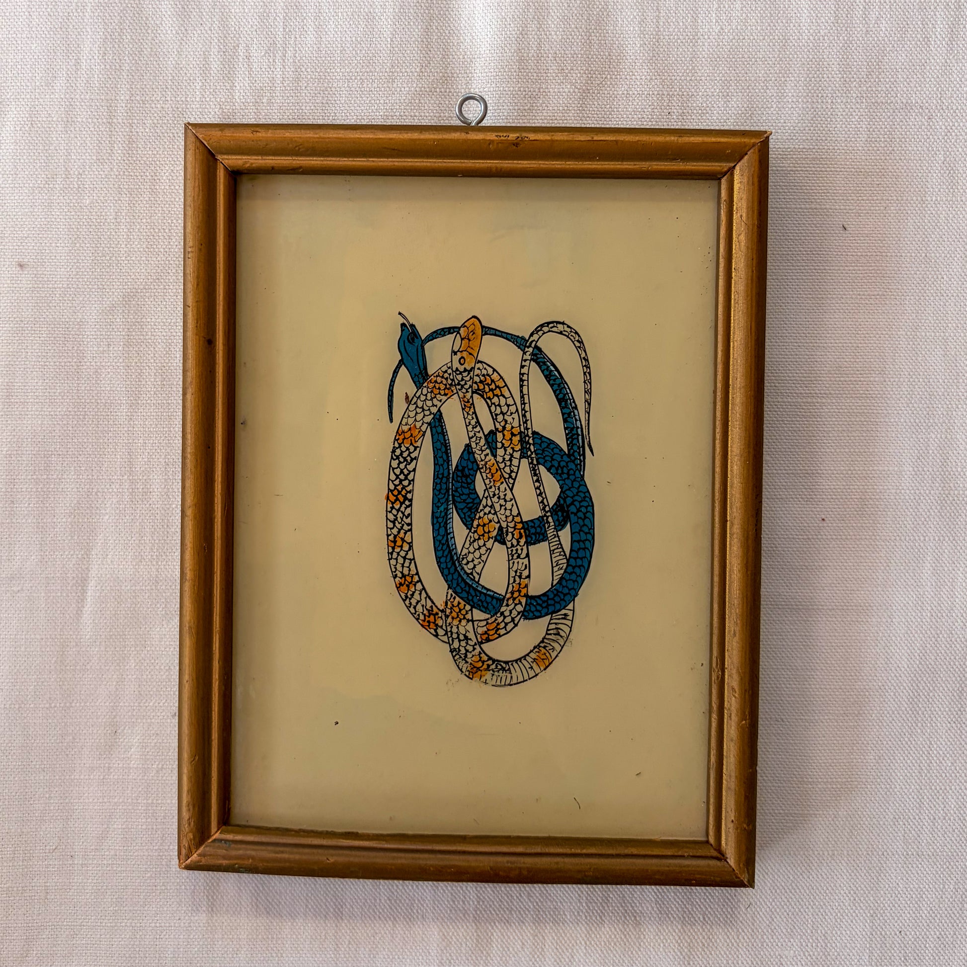 Framed embroidered artwork of interwoven snakes on a beige background