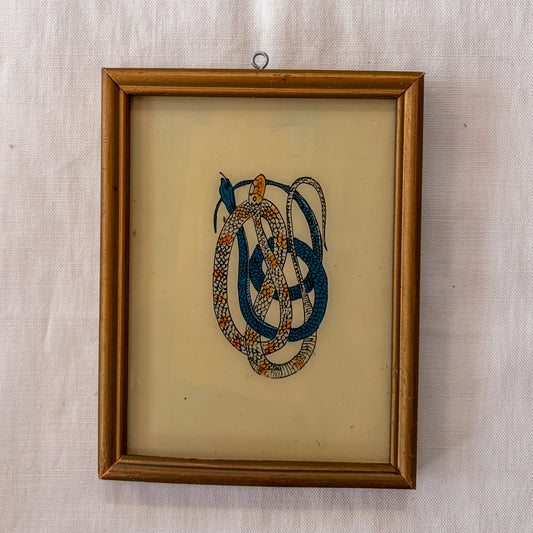Framed embroidered artwork of interwoven snakes on a beige background