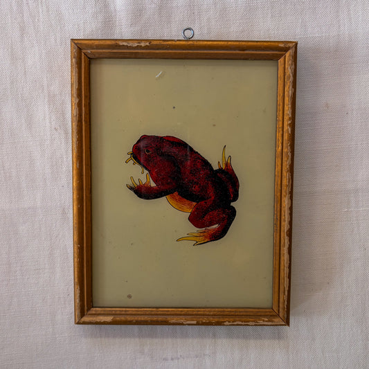 Framed artwork of a red frog with yellow accents on a textured beige background