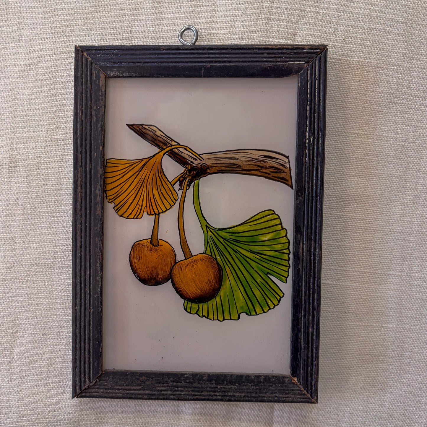 Framed artwork of ginkgo biloba leaves and seeds on a textured wall.