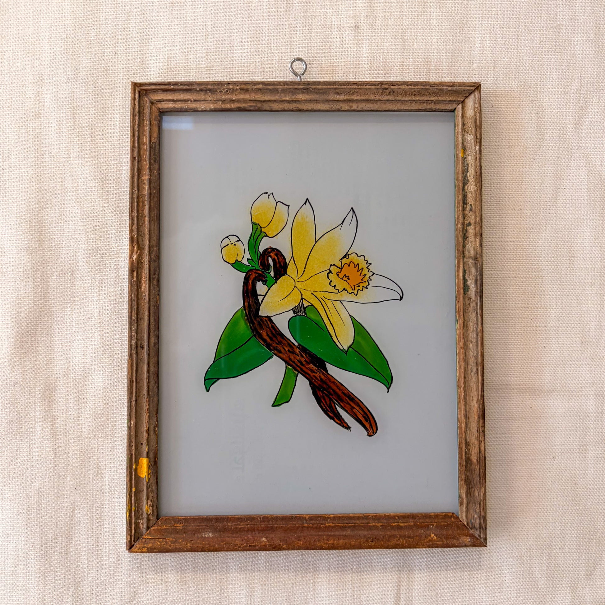 Framed stained glass artwork of a yellow flower and green leaves on a beige background