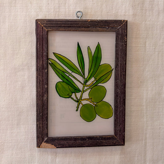 Framed artwork of green leaves and berries on a beige textured wall