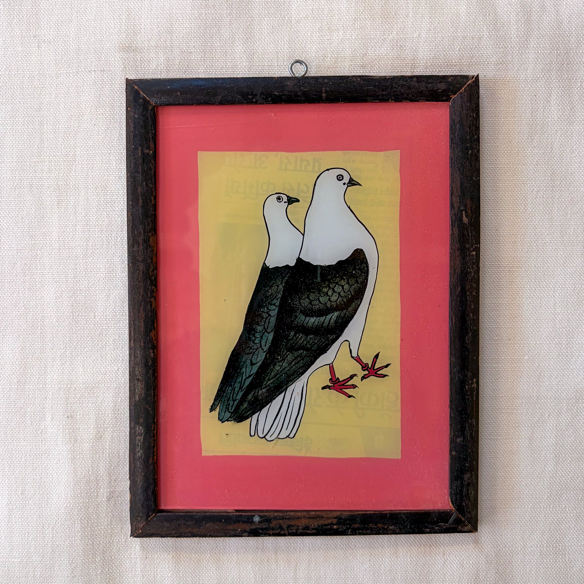 Framed artwork of two birds on a pink background with a textured beige wall.
