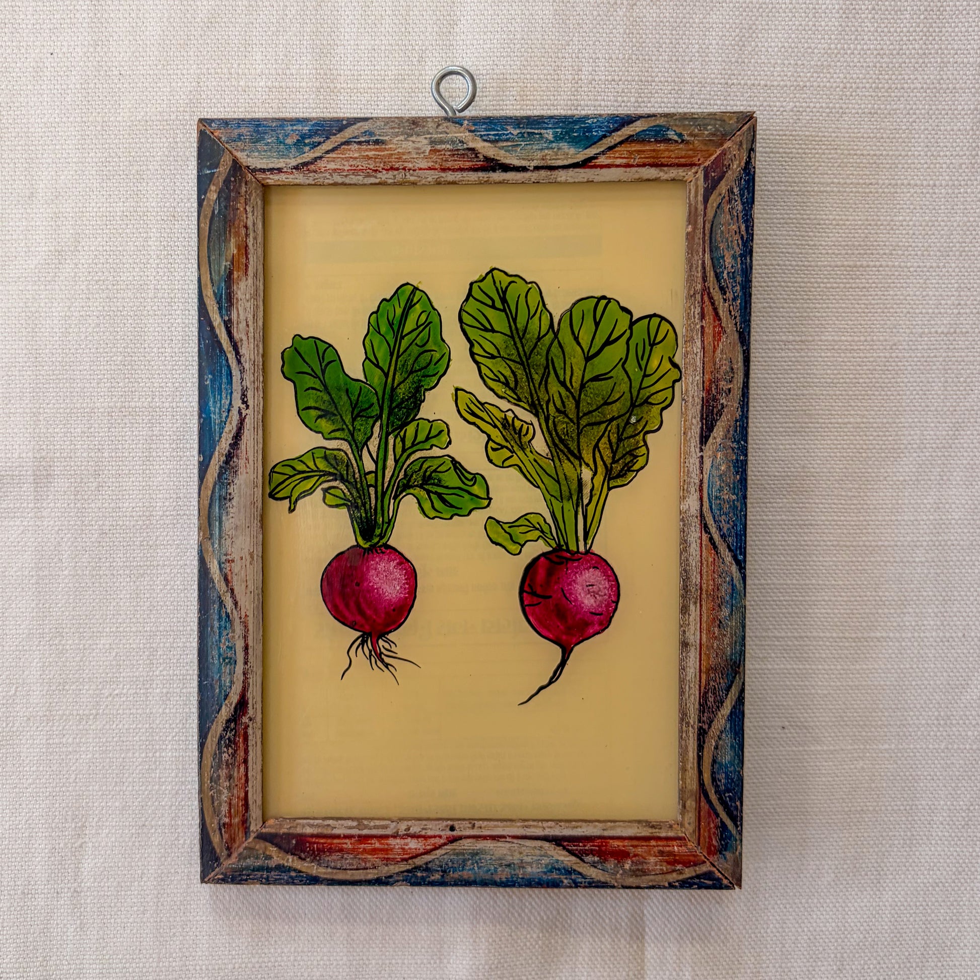 Framed artwork of two radishes with green leaves on a textured wall.