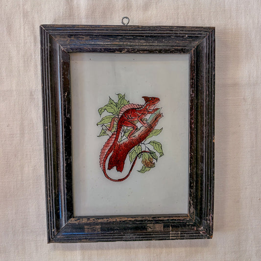 Embroidered red lizard on a white background in a dark wooden frame.