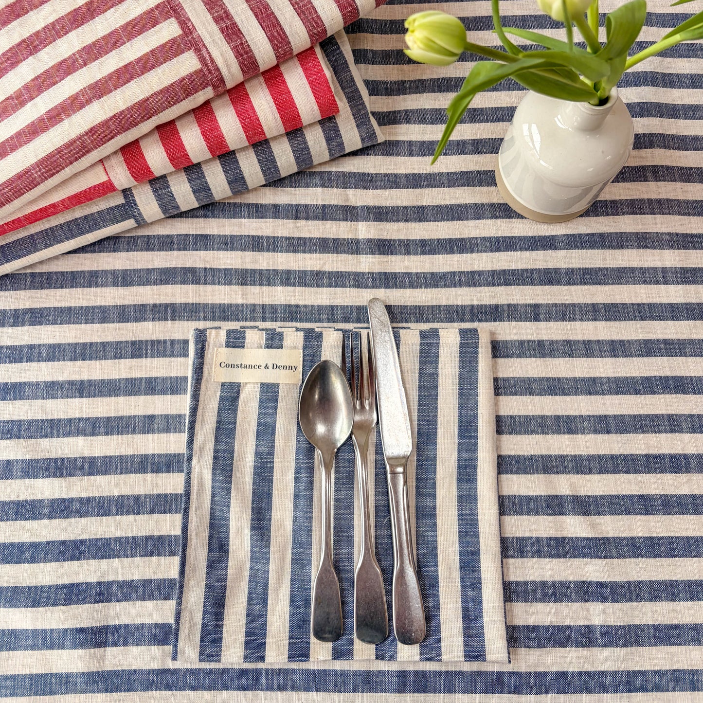 Nautical-themed table setting with striped tablecloth, cutlery, and floral arrangement.