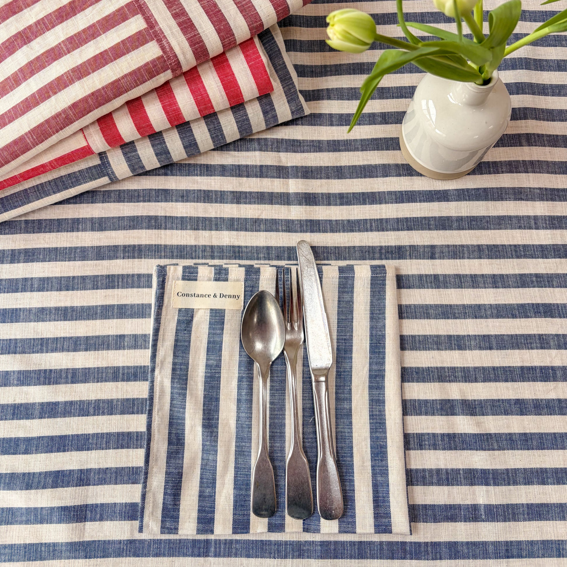 Nautical-themed table setting with striped tablecloth, cutlery, and floral arrangement.