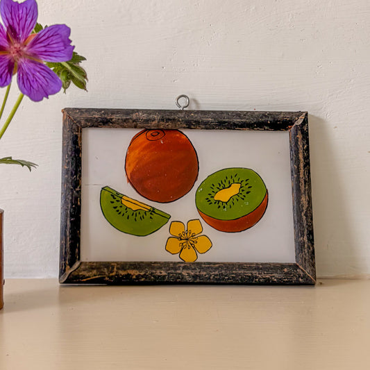 Framed artwork of fruits and a flower on a white wall with a purple flower in the corner.