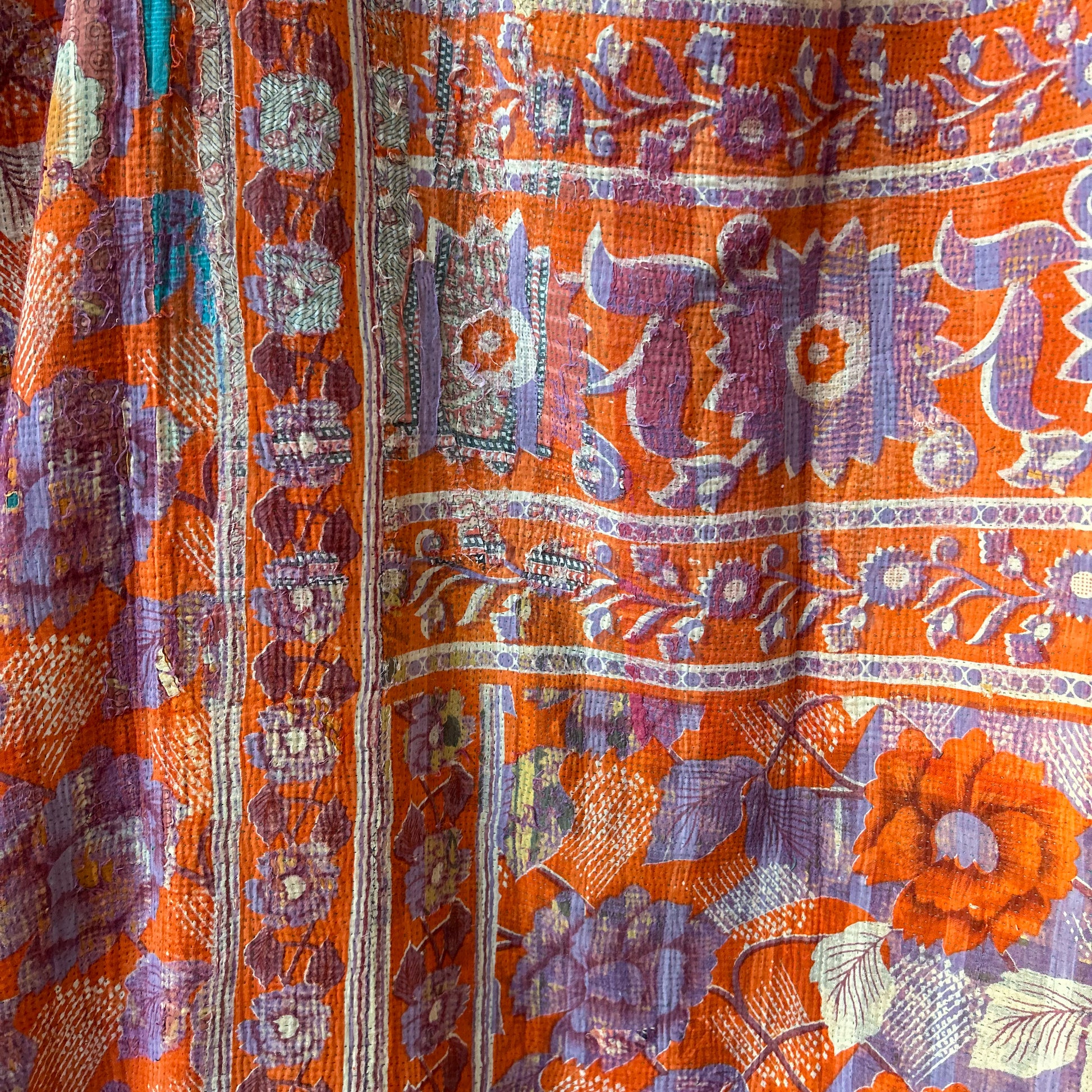 Close-up of a vibrant floral patterned fabric with orange, purple, and green colors. Vintage Kantha. Blanket throw
