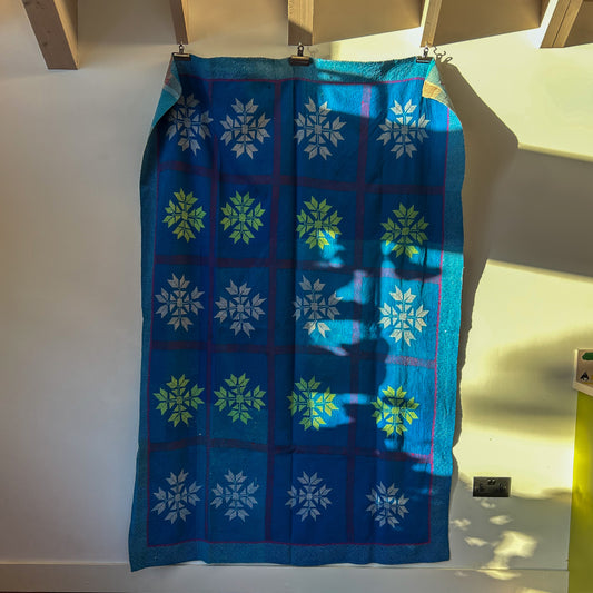 Blue fabric with green and white patterns hanging on a wooden rod.