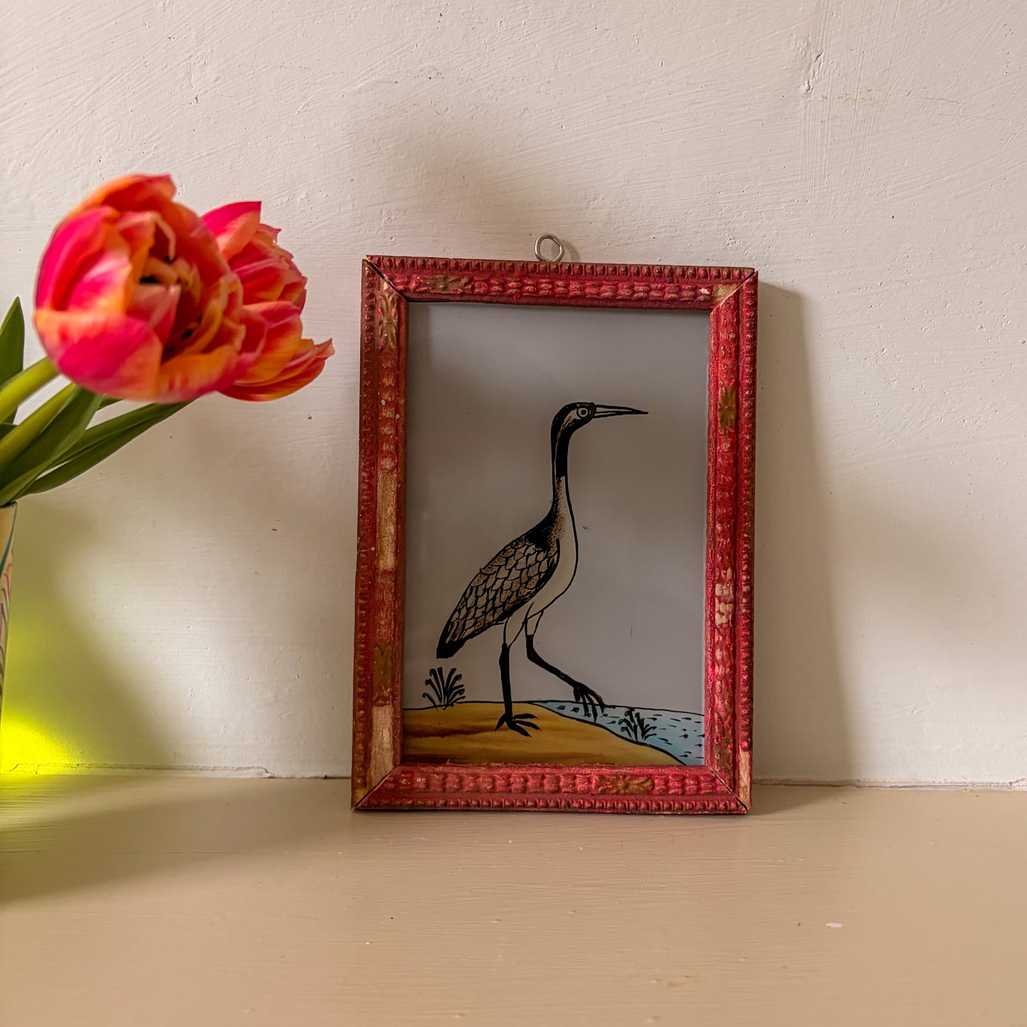 Framed artwork of a bird next to a pink tulip on a wooden surface.