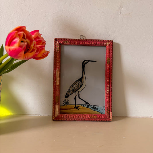 Framed artwork of a bird next to a pink tulip on a wooden surface.