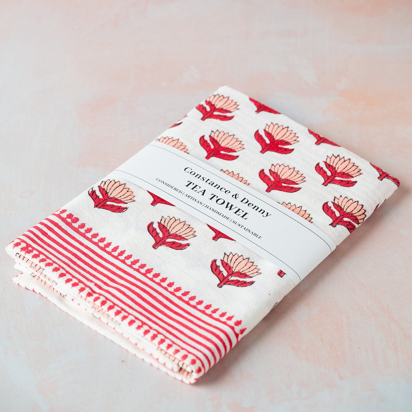 Folded tea towel with red floral pattern on a light pink background