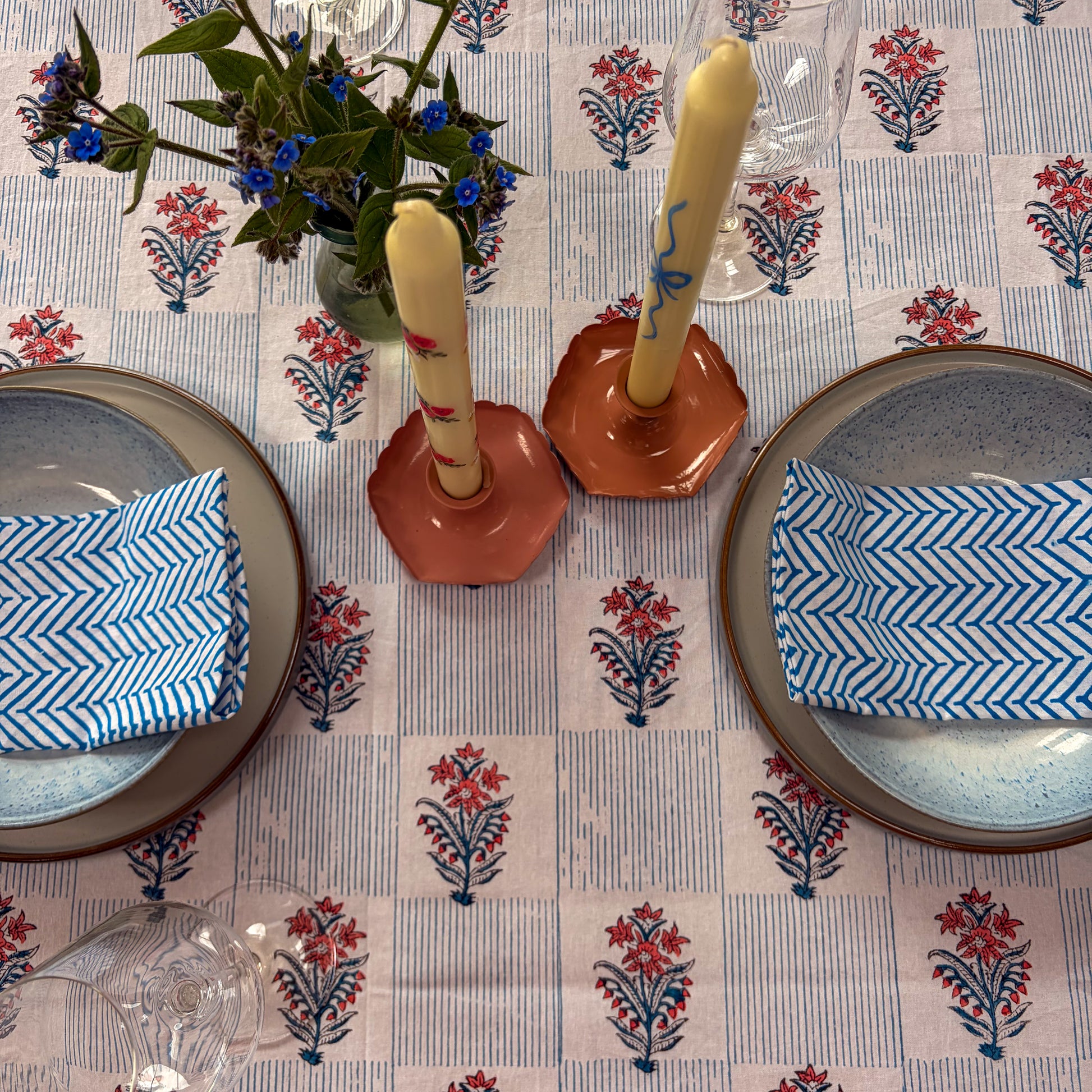 Table setting with floral tablecloth, plates, candles, and napkins.