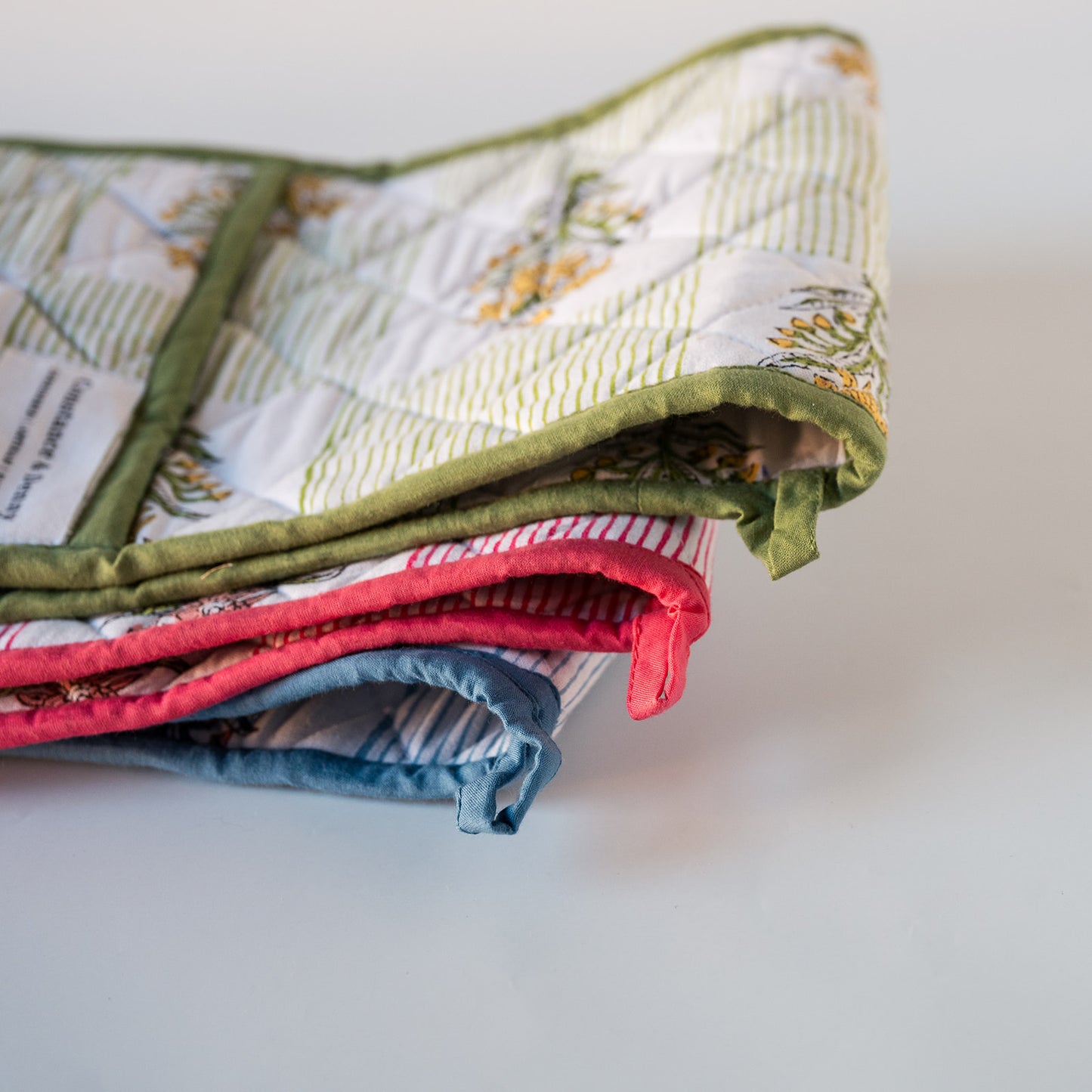A folded quilted oven gloves with a floral and striped pattern in green, white, pink, and blue, shown on a plain light background.