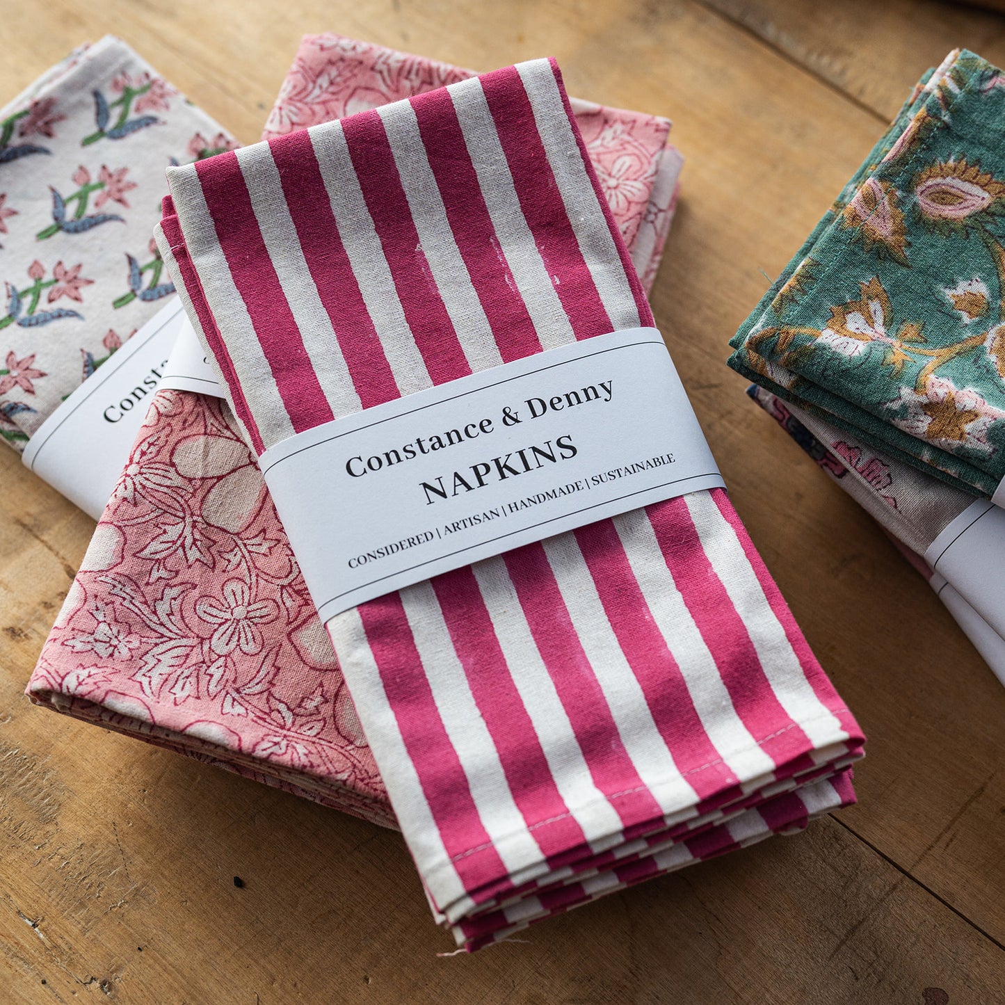 Set of Constance & Denny napkins with floral and striped patterns on a wooden surface.