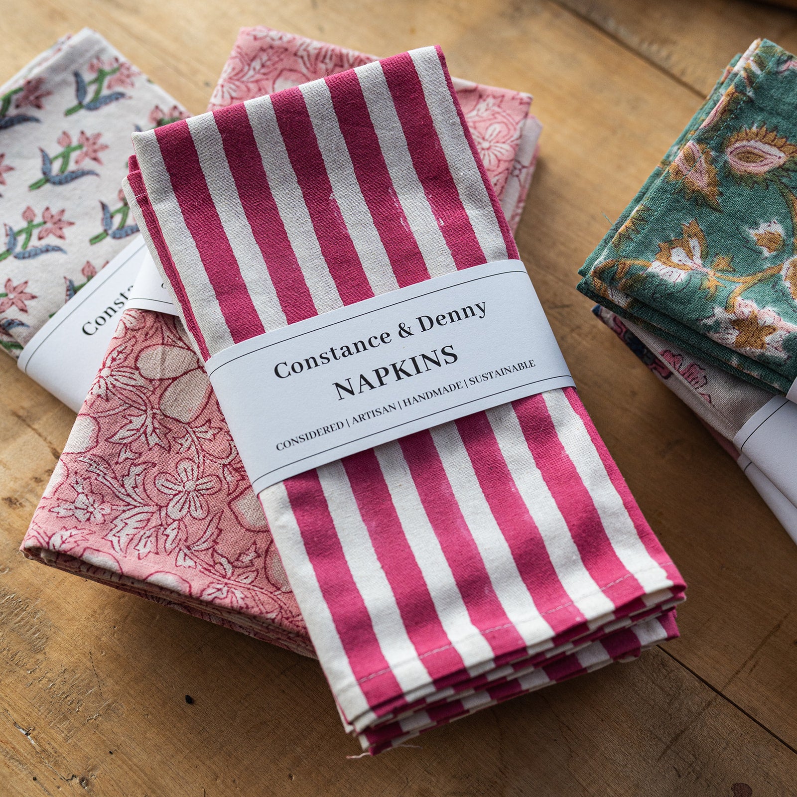 Set of Constance & Denny napkins with floral and striped patterns on a wooden surface.