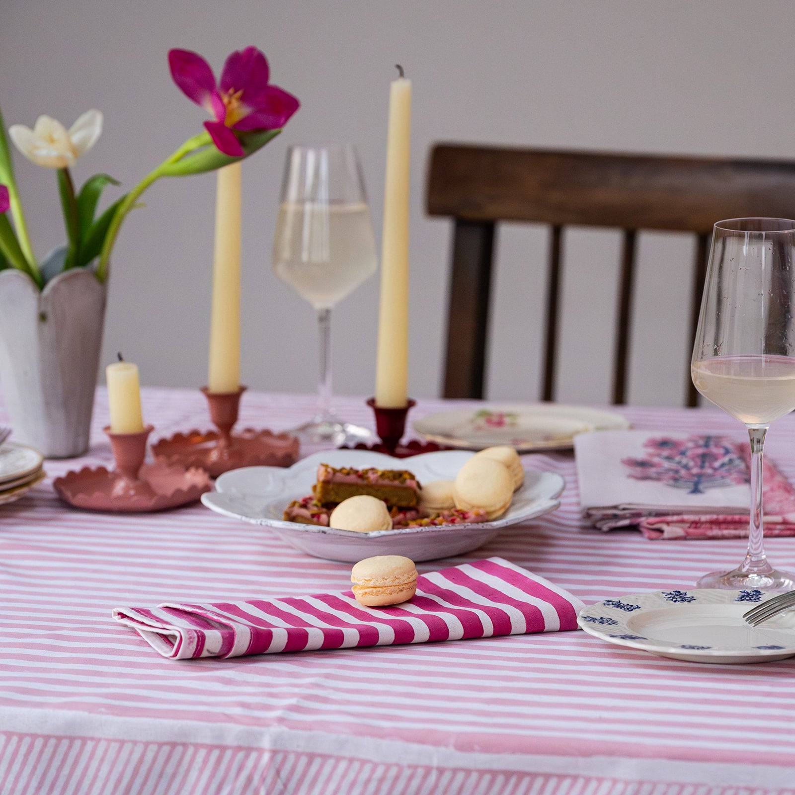 Dining table set with pink tablecloth, candles, flowers, and plates.