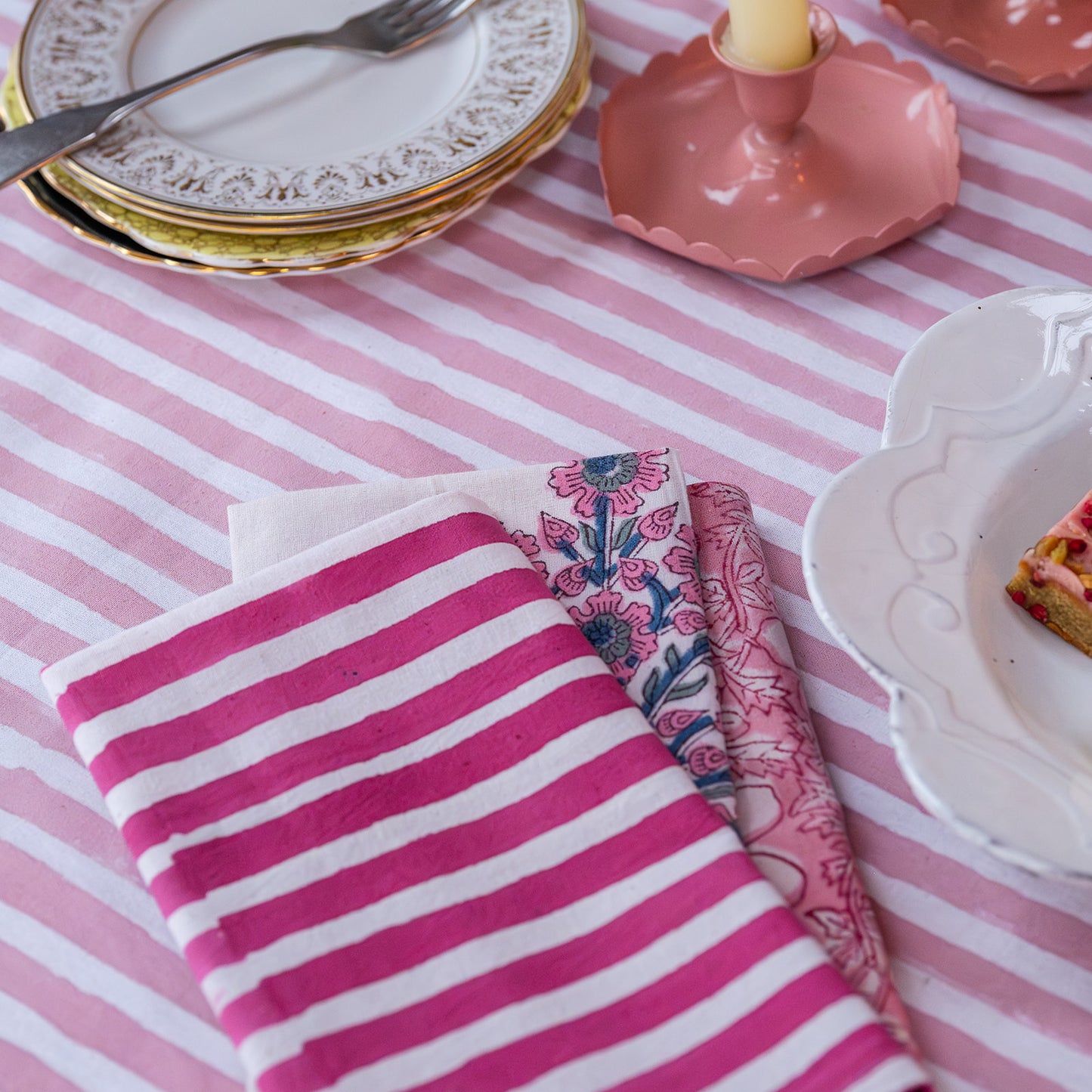 Pink and white striped napkin on a table with decorative plates and cutlery.