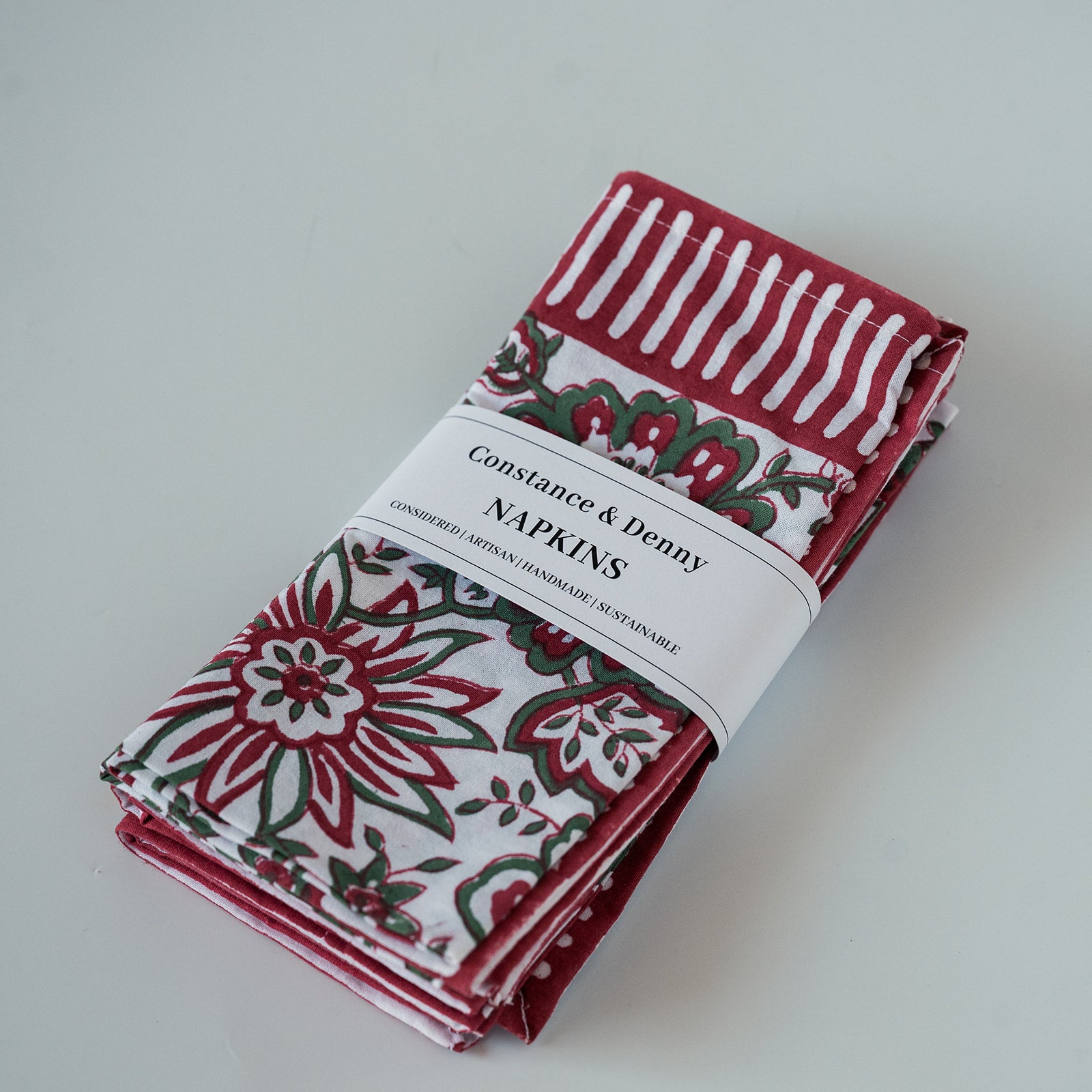 A set of folded patterned napkins wrapped in a white paper band labeled 'Constance & Denny NAPKINS,' photographed on a plain light background.