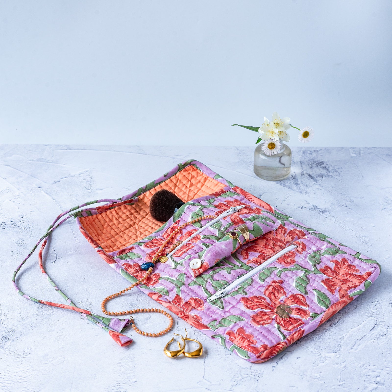 Floral quilted JEWELLERY ROLL with jewelry on a light surface. JEWELLERY-ROLL-BLOCK-PRINTED-QUILTED-CLEMENTINE