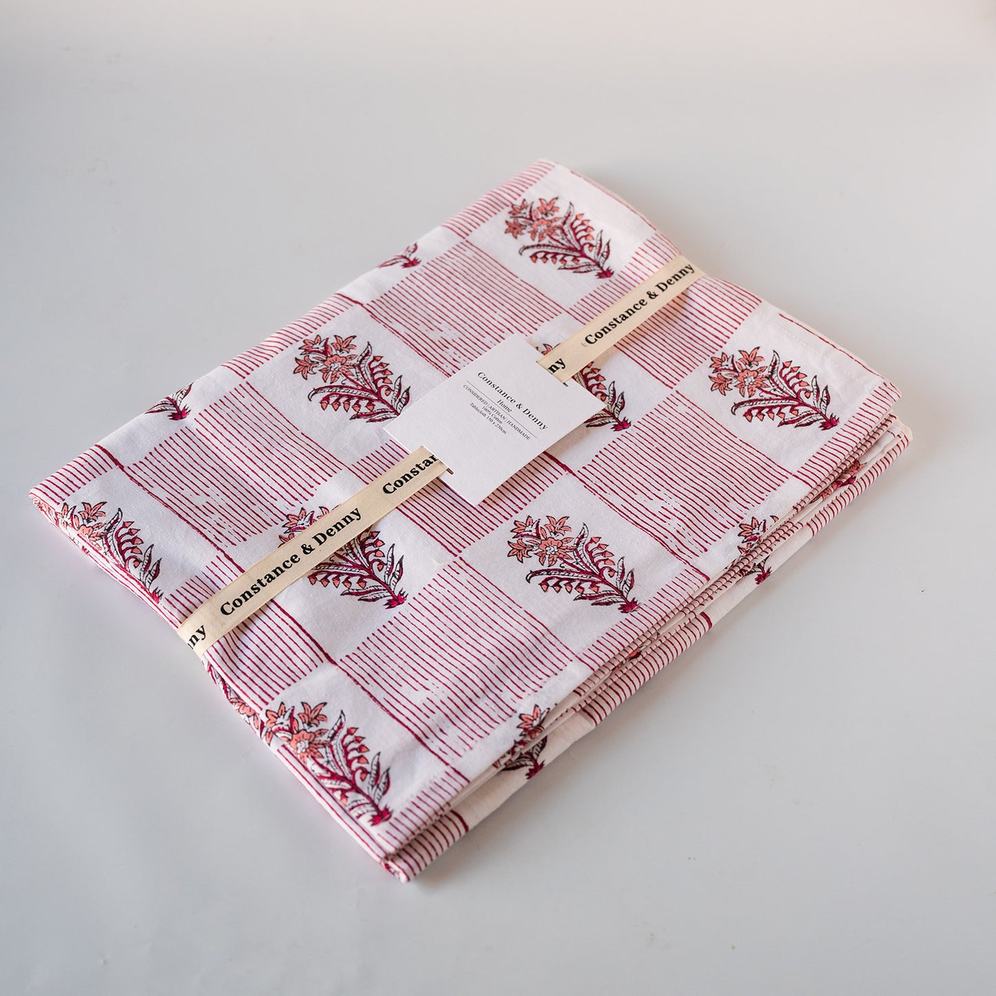 Folded cotton fabric by Constance & Baby, featuring a white base with red stripes and red botanical block prints, wrapped with a paper ribbon.