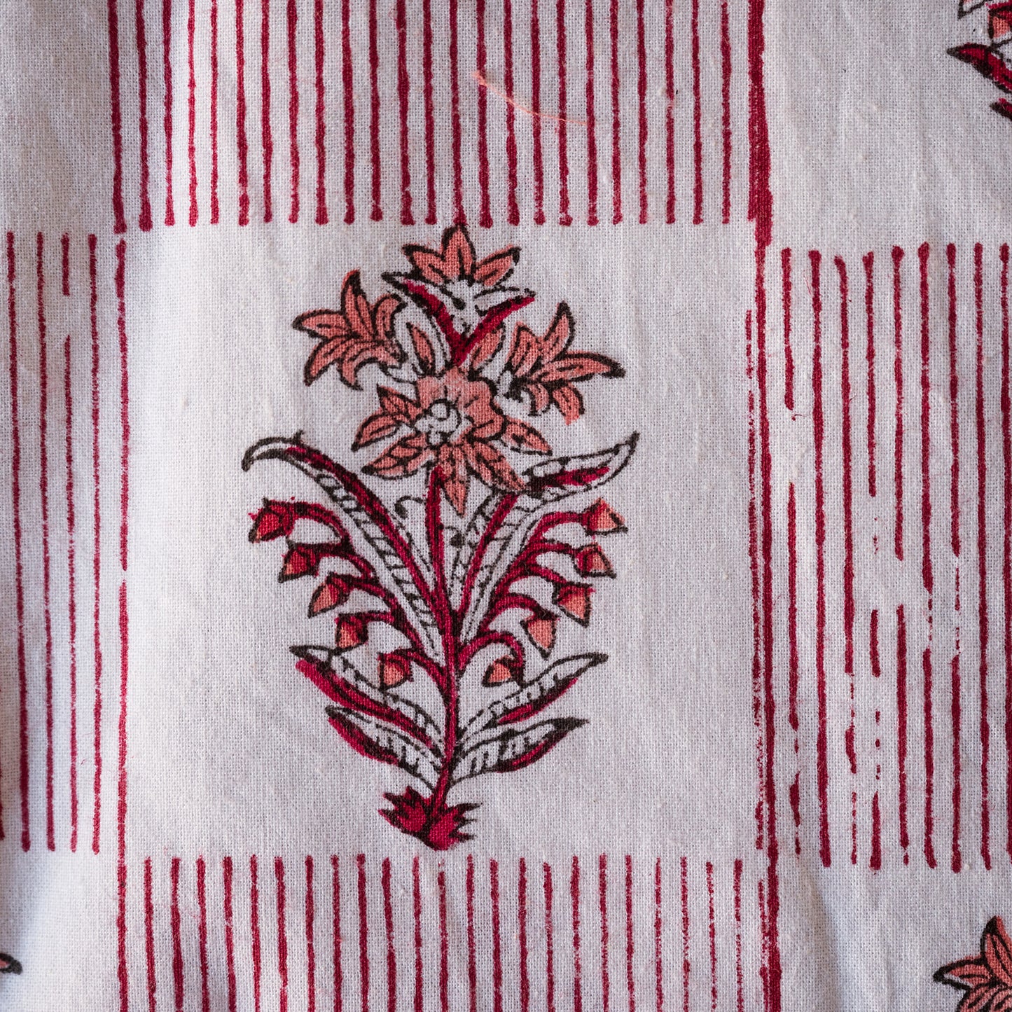 A close-up of white fabric with a red and coral floral block print and vertical red stripe borders.