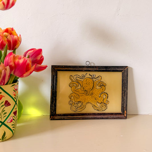 Framed octopus artwork on a shelf with pink tulips in the background