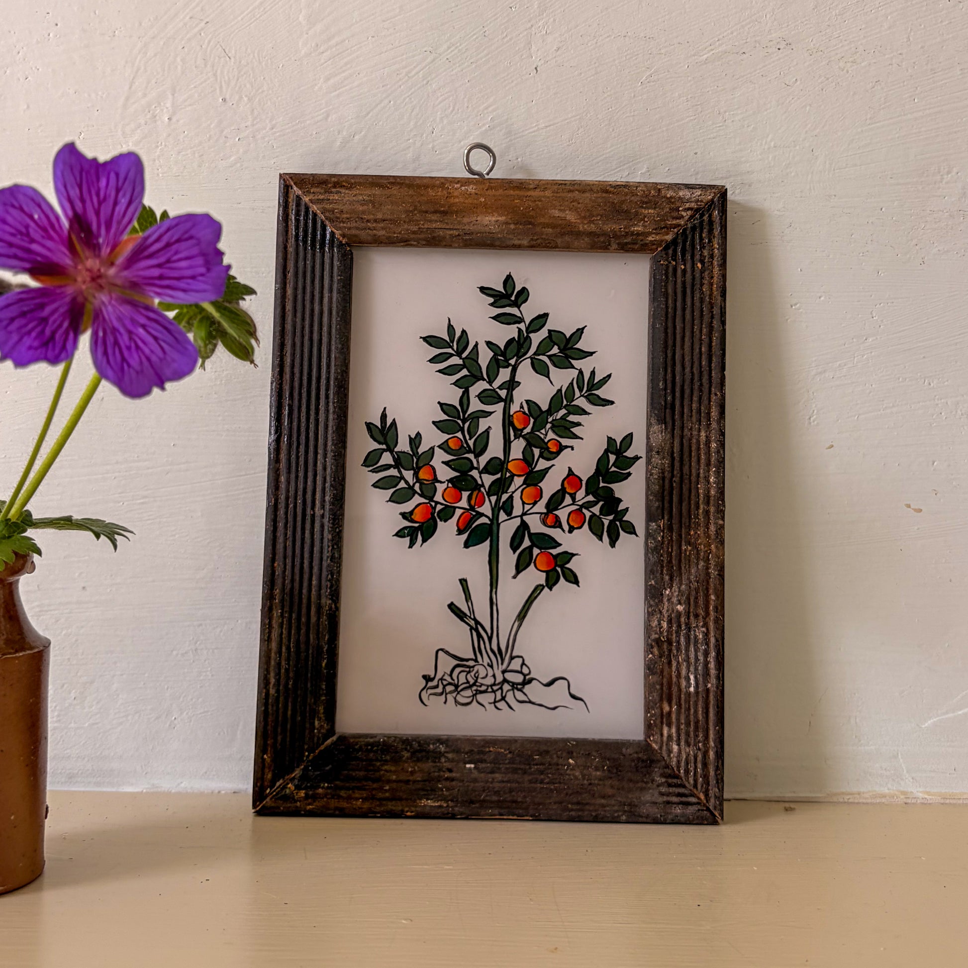 Framed artwork of a plant with berries next to a purple flower in a vase.