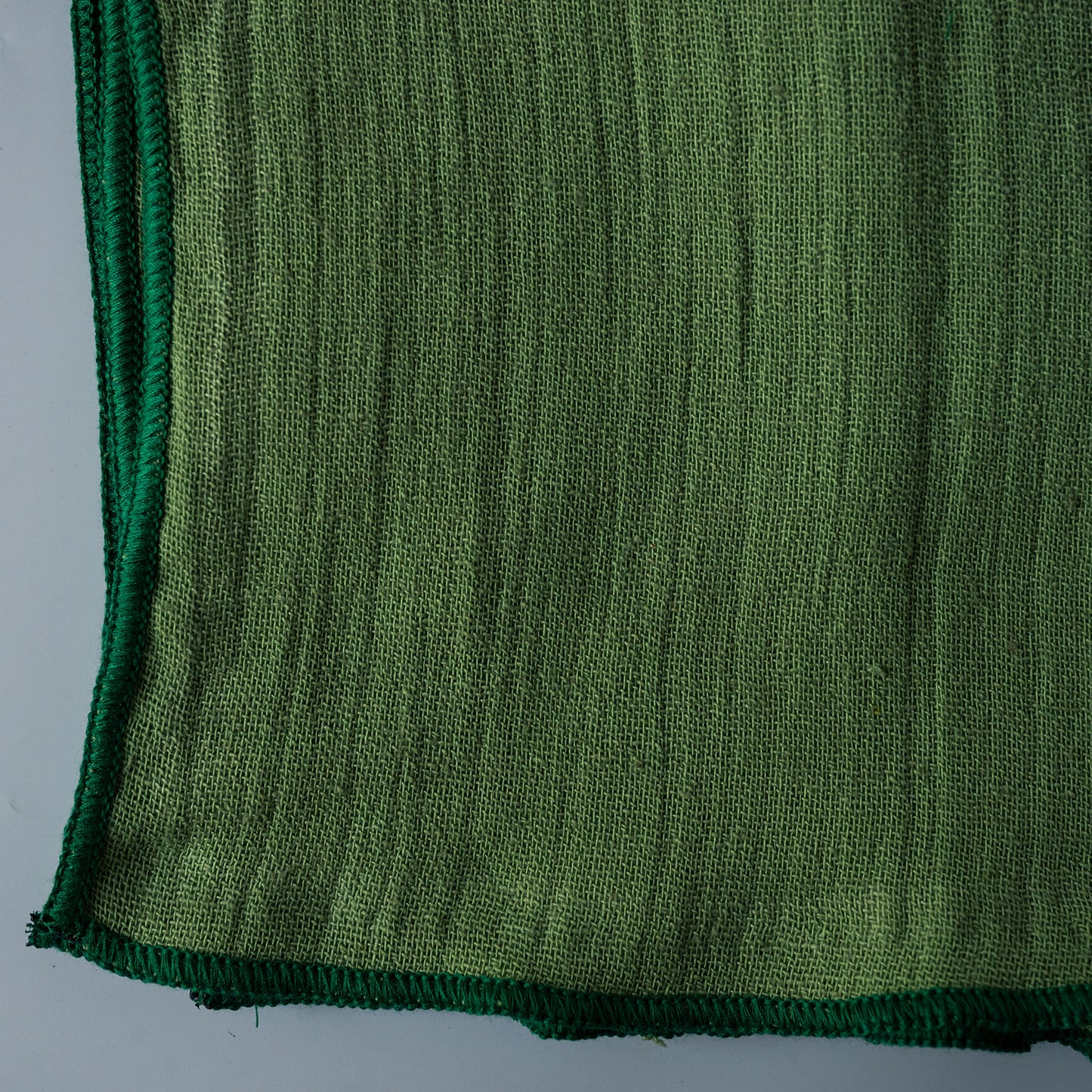 A close-up of a textured olive green woven fabric napkins with a darker green braided border, showing the detailed knit pattern and edges against a light gray background.