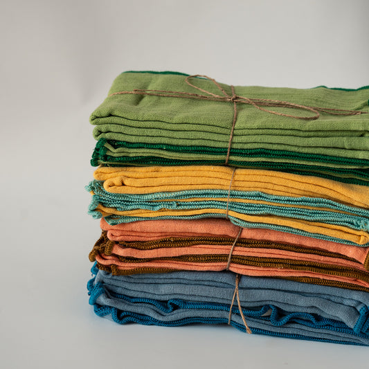 A stack of folded textured fabric napkins in various colors, including green, yellow, orange, brown, and blue, tied together with twine on a light gray background.