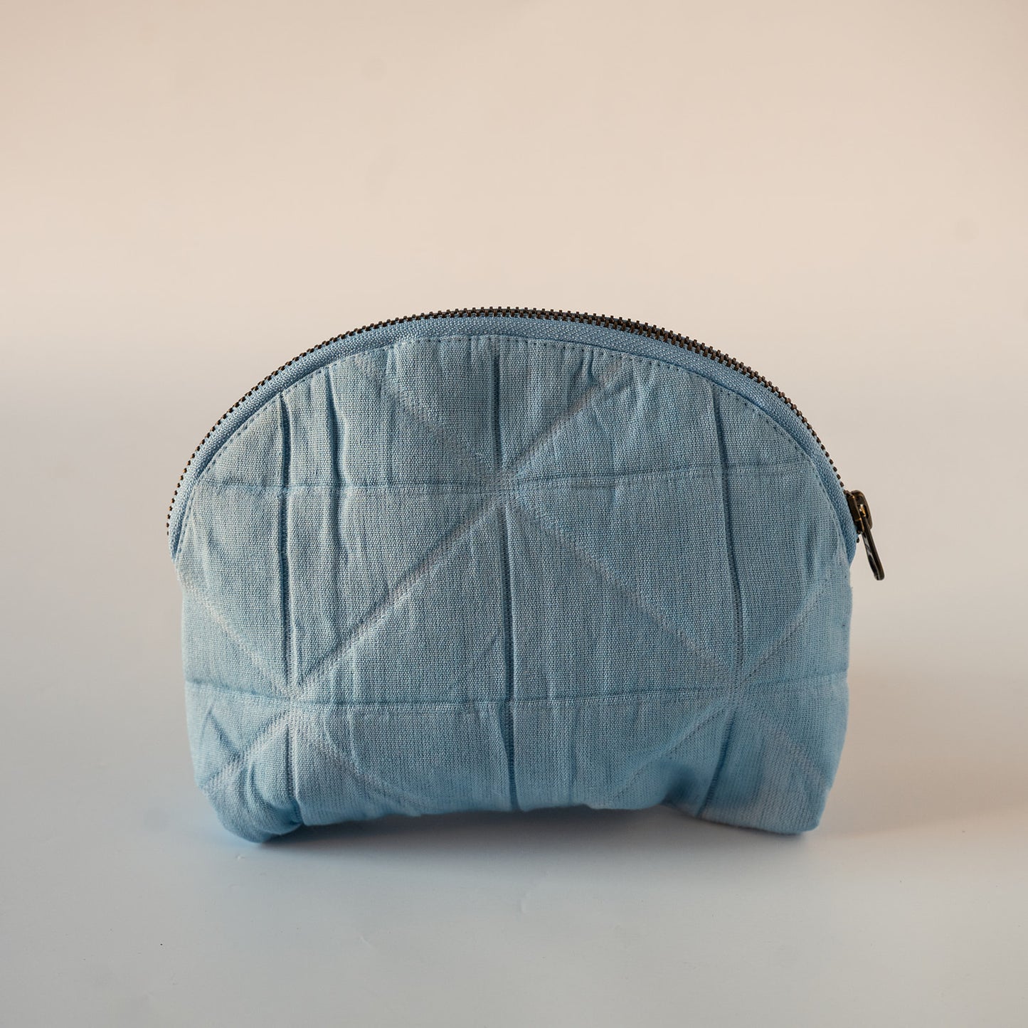 A light blue quilted fabric zippered pouch with a geometric stitched pattern, shown against a plain light beige background.