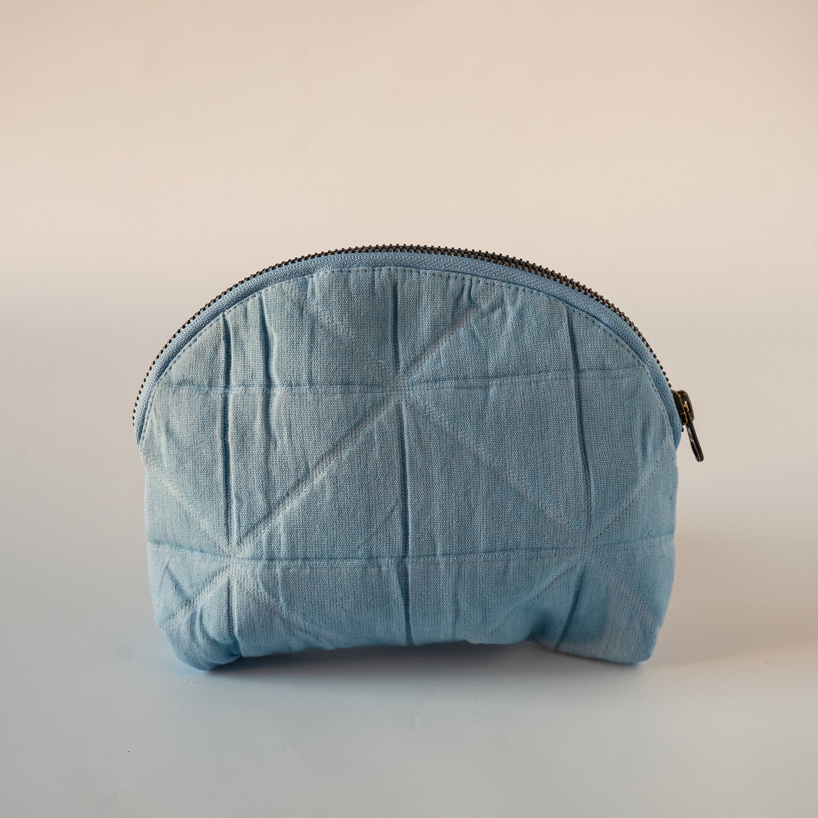A light blue quilted fabric zippered pouch with a geometric stitched pattern, shown against a plain light beige background.