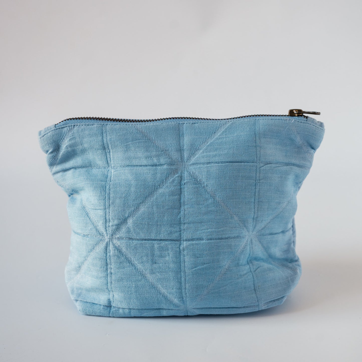 A light blue quilted fabric pouch with a diagonal stitched geometric pattern and a black zipper, shown on a plain light gray background.