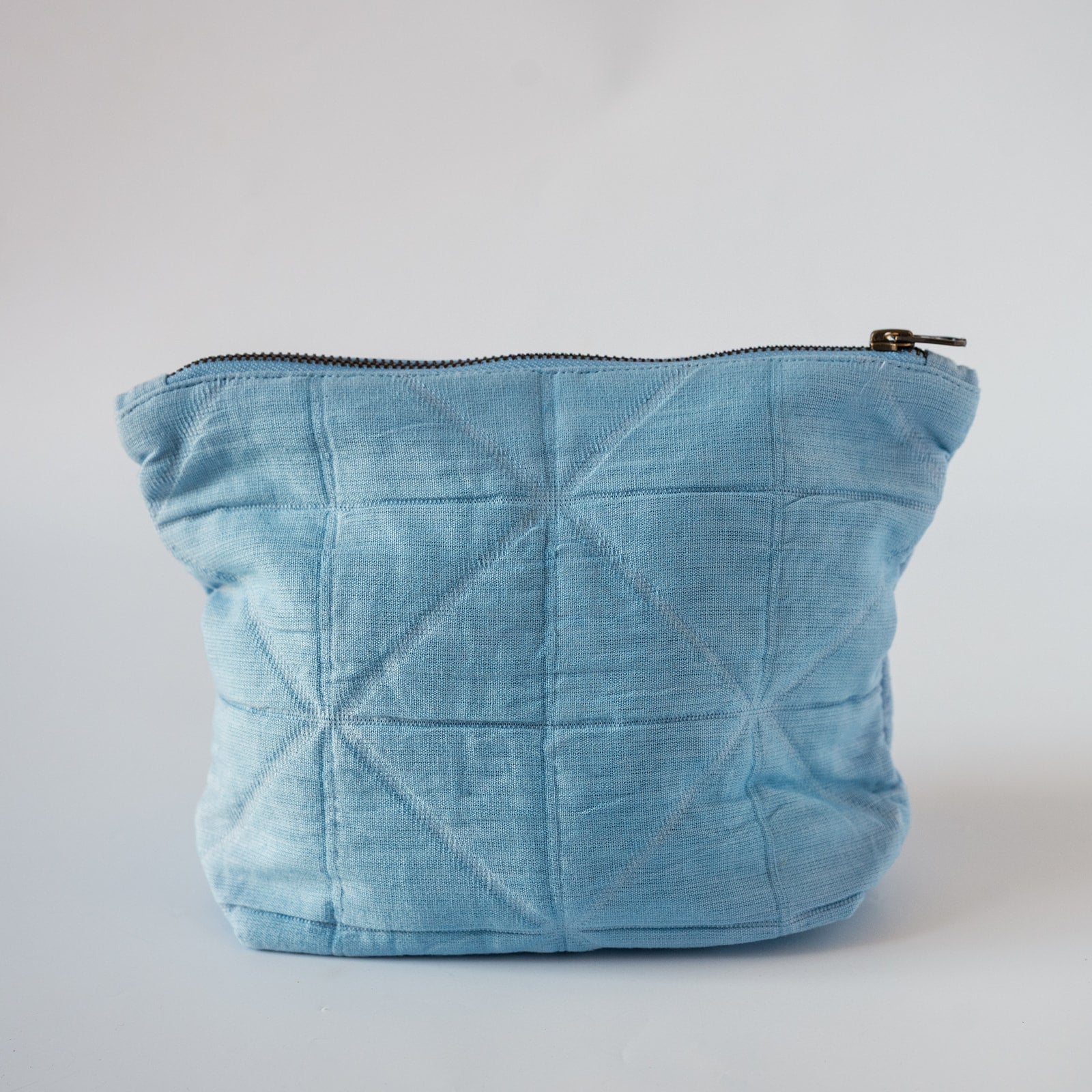 A light blue quilted fabric pouch with a diagonal stitched geometric pattern and a black zipper, shown on a plain light gray background.