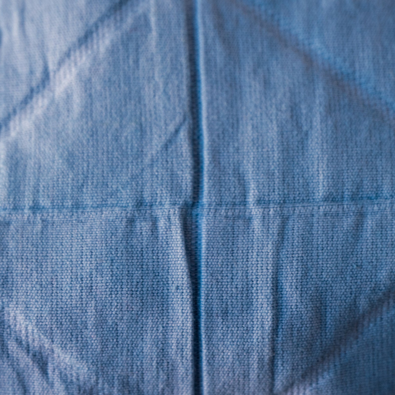 A close-up of a light blue textured fabric with a visible cross seam running through the center.